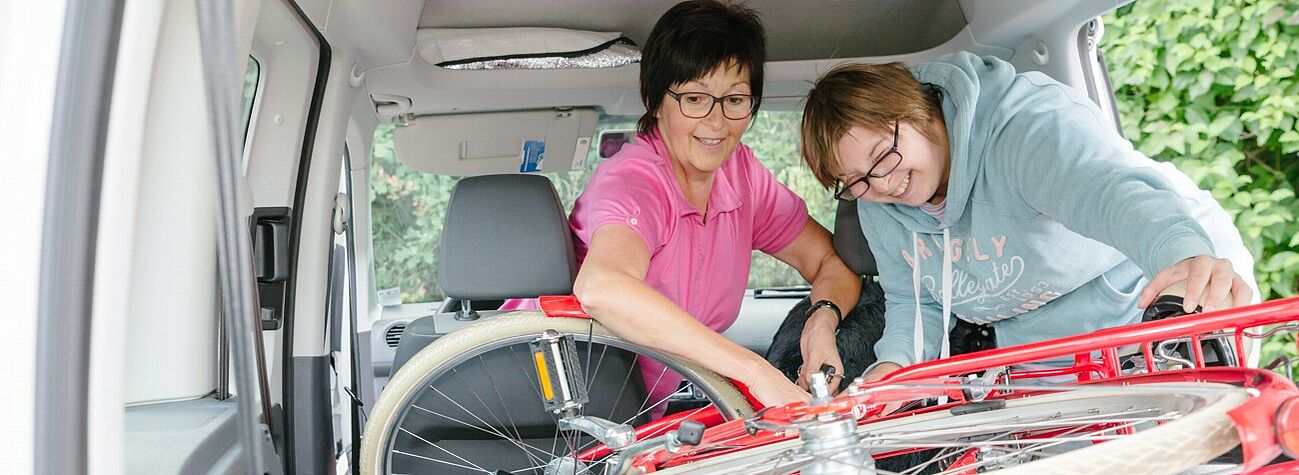 Eine Assistentin der Offenen Hilfen Gunzenhausen hilft einer Klientin beim Verladen des Fahrrads