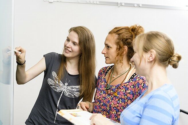 Zwei Schülerinnen und eine Dozentin der Diakoneo Fachschule für Heilerziehungspflege in Nürnberg besprechen den Unterricht an einer Tafel.